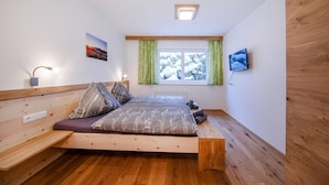 Ein Schlafzimmer mit einem hölzernen Bett, einem fenster mit Vorhängen, einem Wand-Fernseher und einem Gemälde.