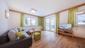 Ein modernes Wohnzimmer mit Sofa, Hocker und Fernseher auf einem Holzboden.