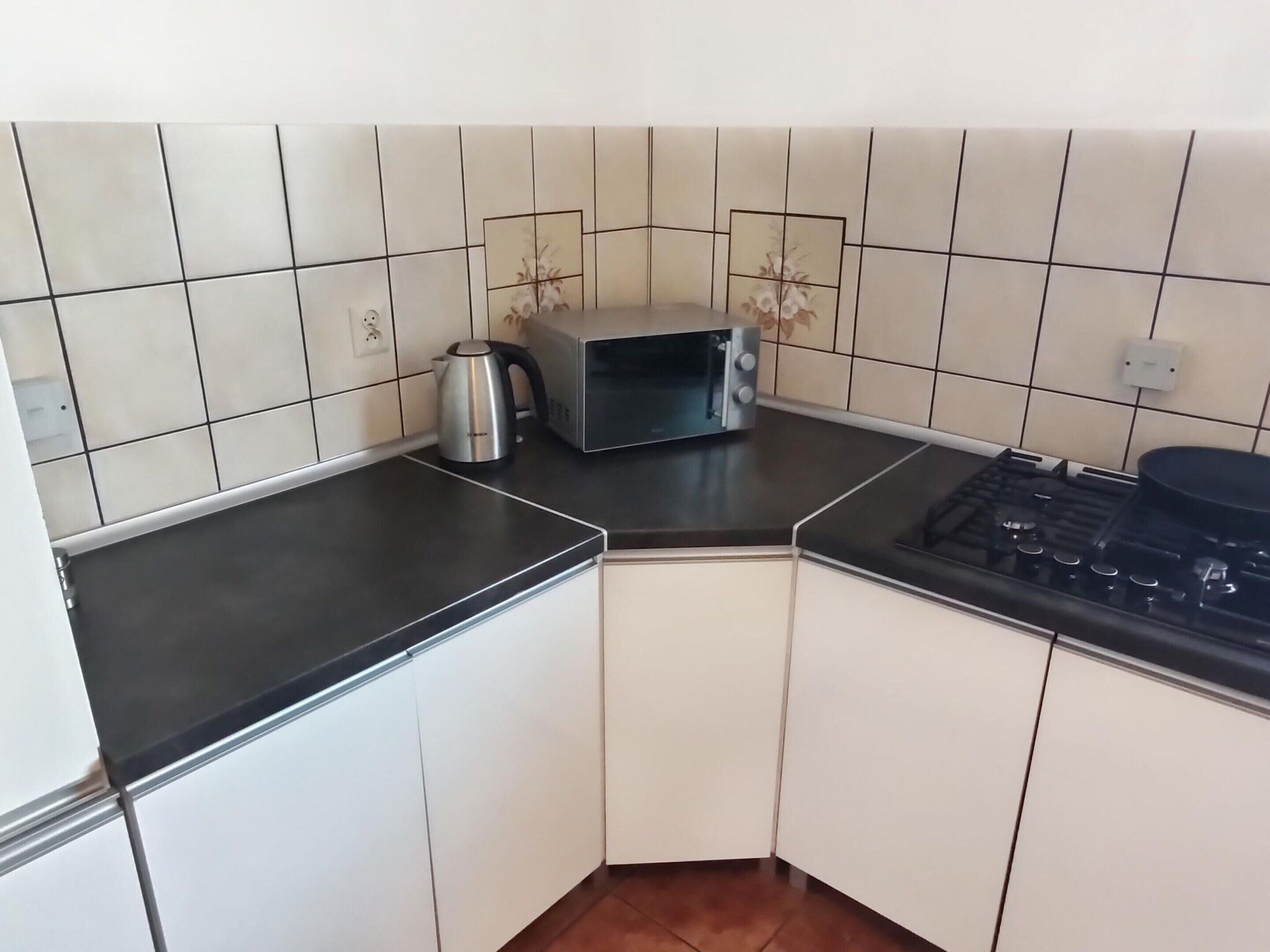 A kitchen with white cabinets, a black countertop, a microwave, a kettle, and a gas stove.