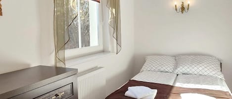Makuuhuone, jossa on sänky, lipasto, ikkuna verhoilla ja seinään kiinnitetty valaisin.