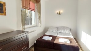 Une chambre à coucher comprenant un lit, une commode, un radiateur, une fenêtre avec des rideaux et un luminaire fixé au mur.