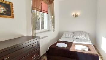 A bedroom with a bed, a dresser, a radiator, a window with curtains, and a wall-mounted light fixture.