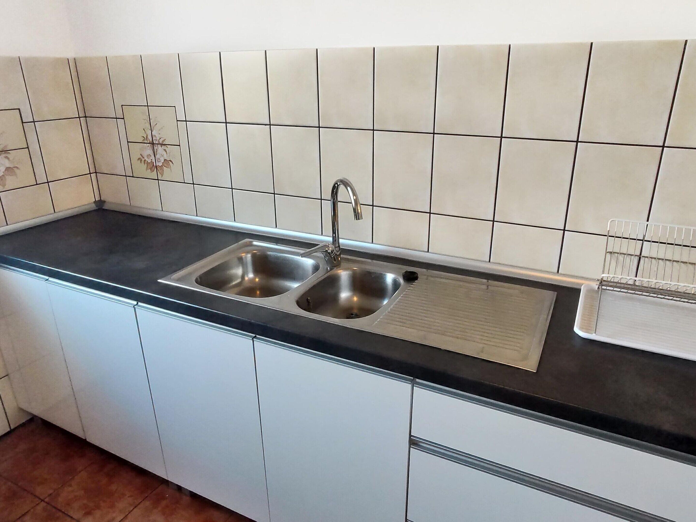 Een keuken met een dubbele roestvrijstalen spoelbak, witte kasten en een zwart aanrecht.