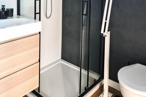 A modern bathroom with a glass shower enclosure, a white toilet, and a wooden vanity.