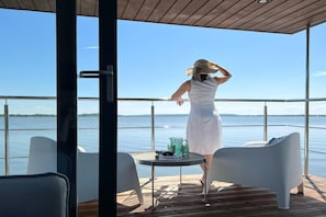 Une personne se tient sur une terrasse surplombant une étendue d’eau, sous un ciel dégagé.