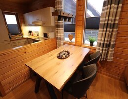 Interior de madeira com mesa de jantar, cadeiras, área de cozinha e janela com cortinas.