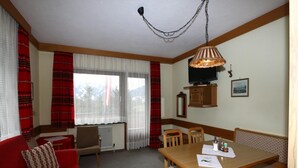 A cozy room with a red sofa, a wooden dining table with chairs, a hanging lamp, and a television on the wall. - Apartment in Vorberg Near Dachstein Glacier (Ramsau am Dachstein)