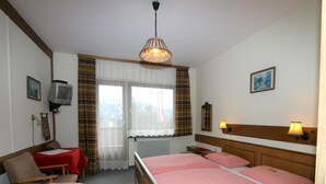 A hotel room with two single beds, a wooden headboard, a desk with a red tablecloth, a television, and a window with curtains. - Apartment in Vorberg Near Dachstein Glacier (Ramsau am Dachstein)