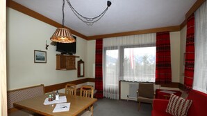 A room with a wooden dining table, chairs, a red sofa, a TV, and a window with curtains. - Apartment in Vorberg Near Dachstein Glacier (Ramsau am Dachstein)