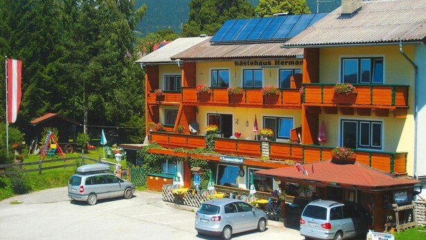A multi-story building with a yellow facade, balconies with flower boxes, and a sign reading "Gastehaus Herman Apartments." - Apartment in Vorberg Near Dachstein Glacier (Ramsau am Dachstein)