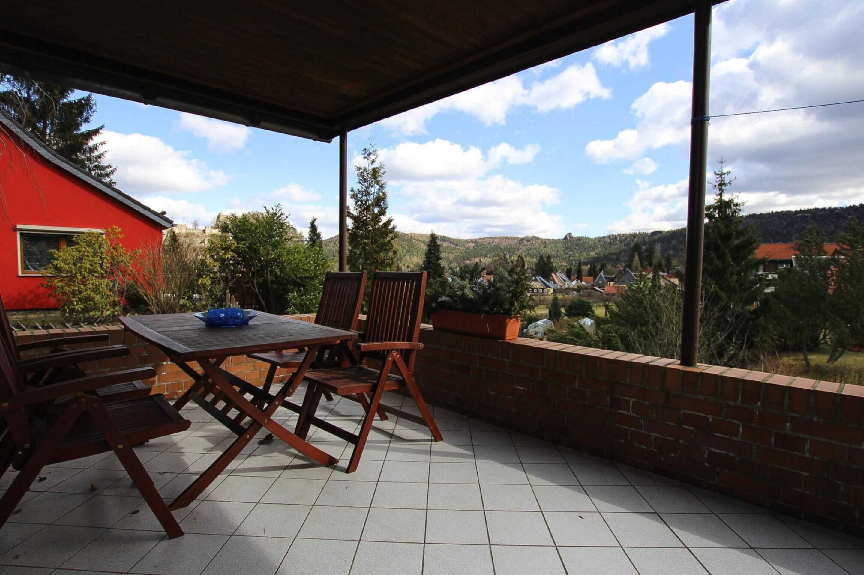 A covered patio with a table and chairs, a brick wall, and a view of a red building and hills.