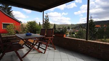 A covered patio with a table and chairs, a brick wall, and a view of a red building and hills.