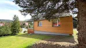 Une petite maison en bois avec deux fenêtres, entourée d’une pelouse et d’arbres.