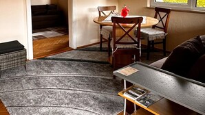 Une pièce comprenant une table à manger, des chaises, un canapé, une petite table avec un plateau, un ventilateur de plafond et une fenêtre avec des stores.