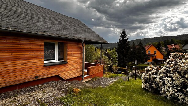 Une maison en bois avec un porche, une fenêtre et un jardin fleuri.