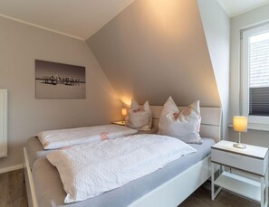 A bedroom with a bed, two bedside tables, a nightstand, a lamp, and a wall-mounted picture. - Ferienwohnung Dunenzauber (St. Peter-Ording)