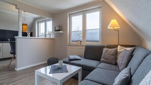 A modern living room with a grey sofa, a white coffee table, and a lamp. - Ferienwohnung Dunenzauber (St. Peter-Ording)
