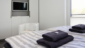 Une chambre d’hôtel moderne, équipée d’un lit, d’un téléviseur fixé au mur, d’une chaise blanche et d’une fenêtre donnant sur un beau paysage.