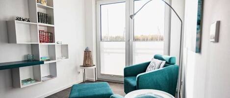 A modern living room with teal sofas, a white coffee table, and a white bookshelf.