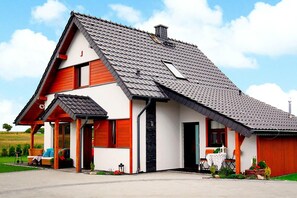 Una casa a due piani con tetto spiovente, un camino e un piccolo garage adiacente.