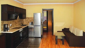 A modern kitchen with dark cabinets, a stainless steel refrigerator, and a coffee maker. There is a wooden floor and a dark-colored sofa in the living area. - Comfortable Holiday Home With Summer Pool + Sauna (gmina Sianów)