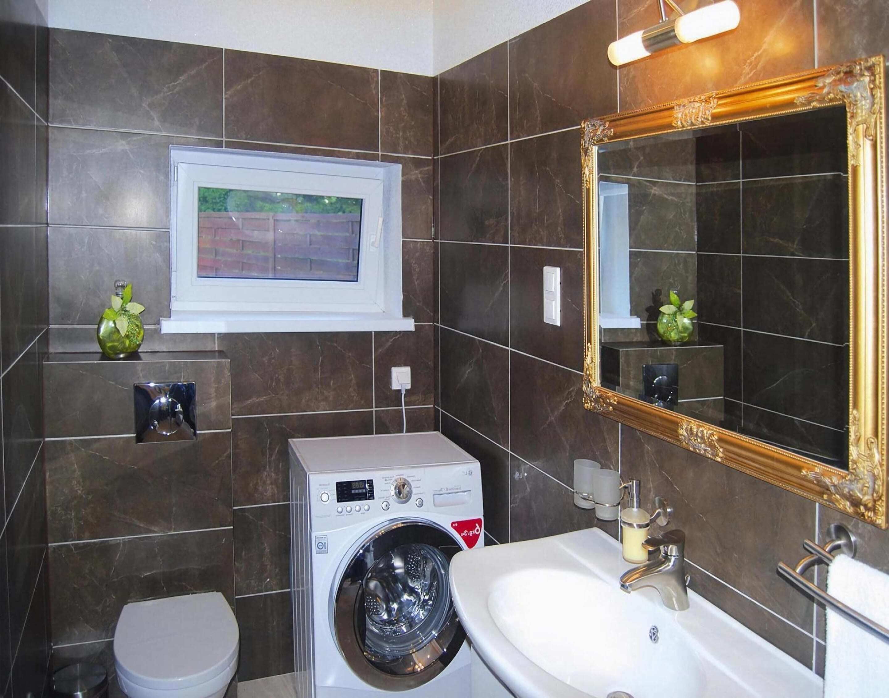 Une salle de bain équipée d’un lave-linge, de toilettes, d’un lavabo et d’un grand miroir agrémenté d’un cadre décoratif.