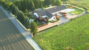 An aerial view of a residential area with a large house featuring a swimming pool, a fenced yard, and adjacent fields. - Comfortable Holiday Home With Summer Pool + Sauna (gmina Sianów)