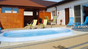 A swimming pool with lounge chairs, a wooden building with a tiled roof, and a white wall with a window. - Comfortable Holiday Home With Summer Pool + Sauna (gmina Sianów)