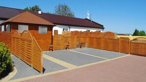 A fenced outdoor area with a paved walkway, a building with a red roof, and a satellite dish. - Comfortable Holiday Home With Summer Pool + Sauna (gmina Sianów)