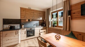 A modern kitchen with wooden cabinets, a built-in oven, and a dining area with a wooden table and chairs. - Apartment in Brixental (Brixen im Thale)