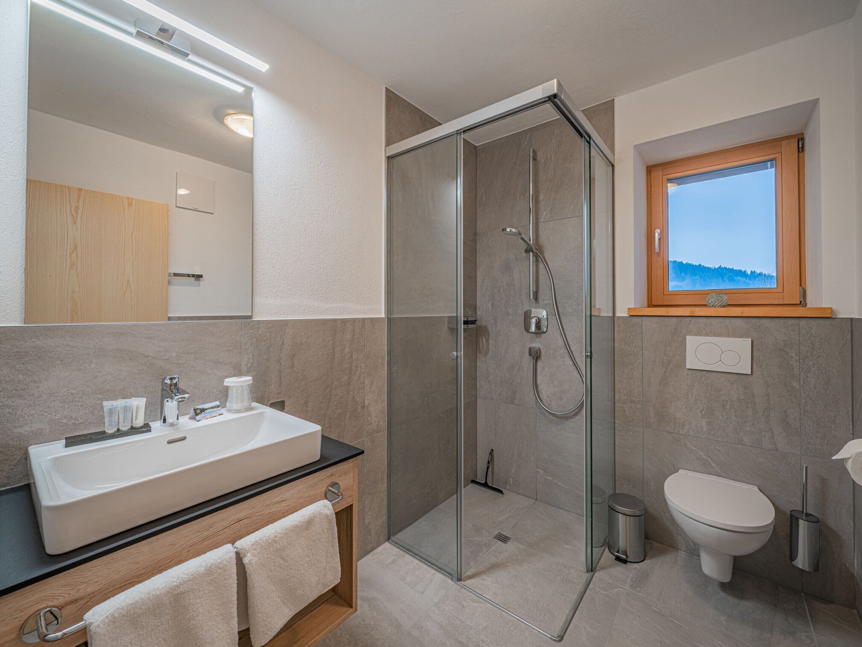 Un baño moderno con ducha de vidrio, lavamanos con artículos de aseo y retrete.