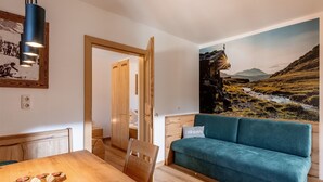 A cozy room with a wooden dining table, a teal sofa, and a mural of a mountainous landscape. - Apartment in Brixental (Brixen im Thale)