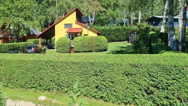 Ett gult hus med ett rött tak, omgivet av välskötta häckar och träd.