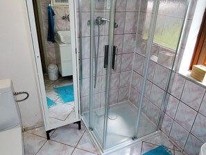 Eine gläserne Dusche mit gefliestem Boden und einem weißen Waschbecken im Hintergrund.