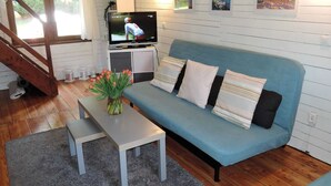 Ett mysigt vardagsrum med en blå soffa, ett litet bord med en vas med blommor, en tv och en trappa.