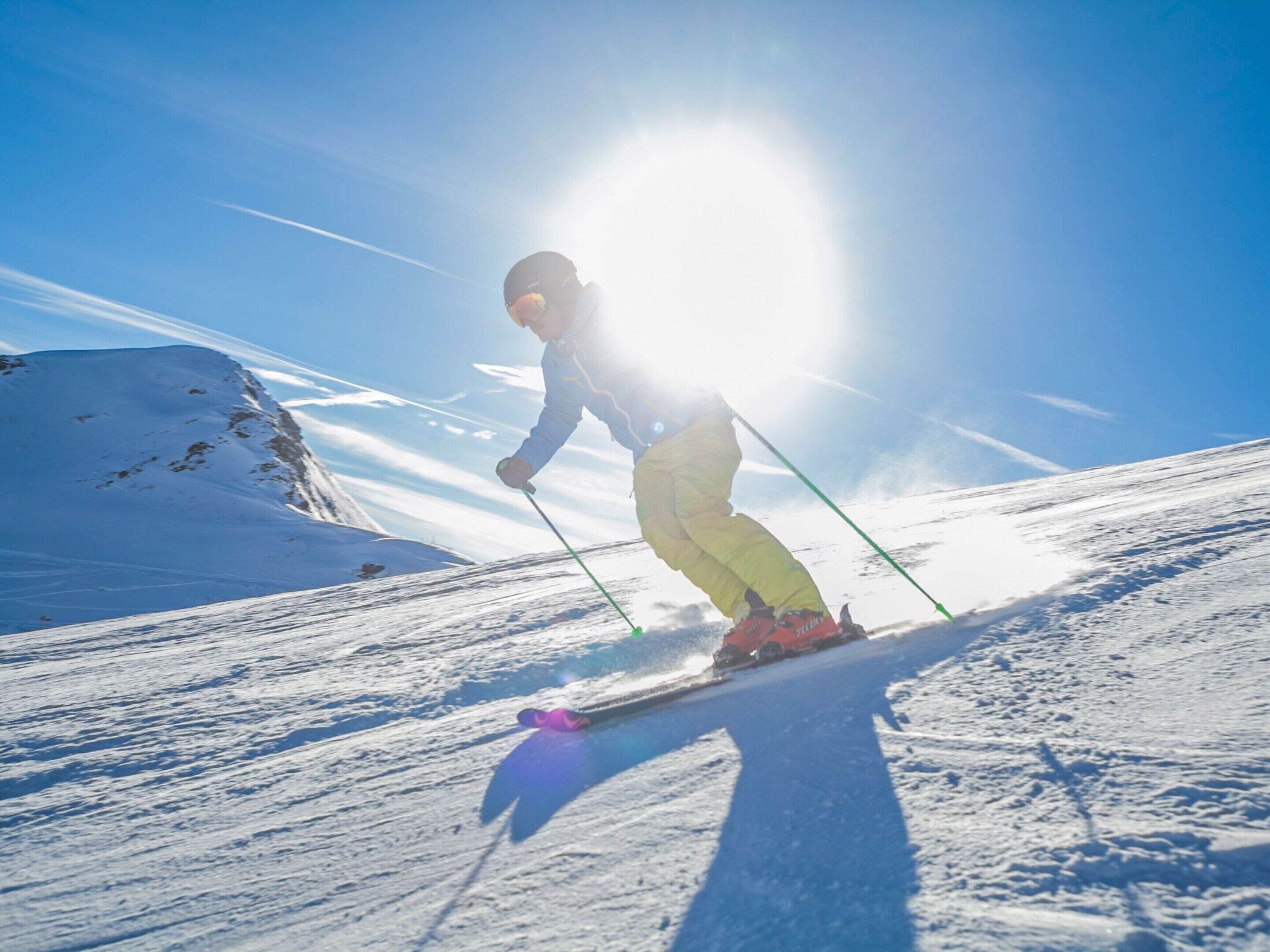 A person skiing down a snowy slope with the sun shining brightly in the background.