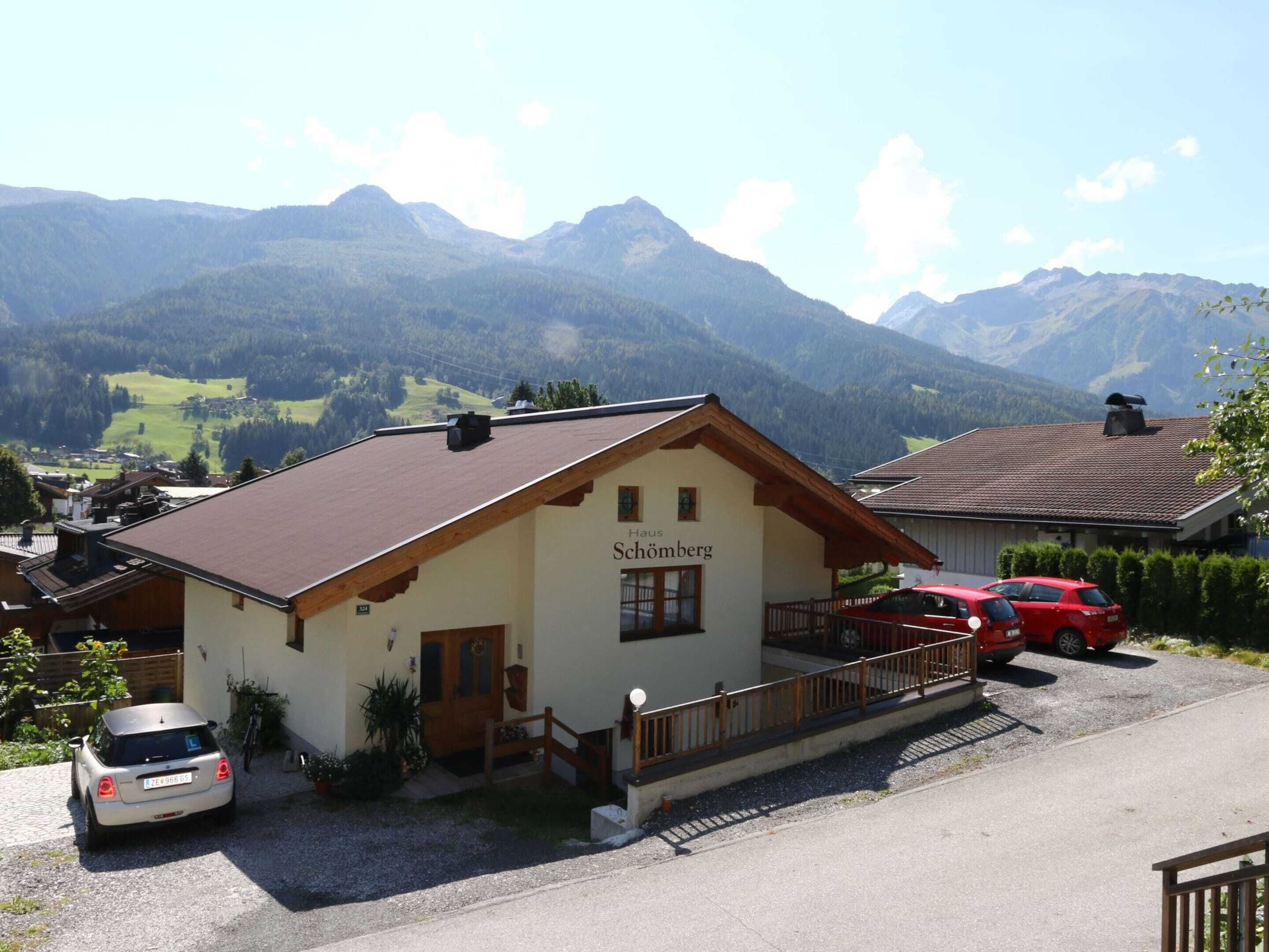 A building labeled "Haus Schömburg" with a red car parked in front, surrounded by mountains.