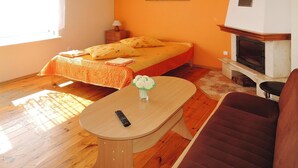A room with a bed, a small table with a vase, a chair, a nightstand, a lamp, and a fireplace. - Holiday Home in Kolczewo by the Lake (gmina Wolin)