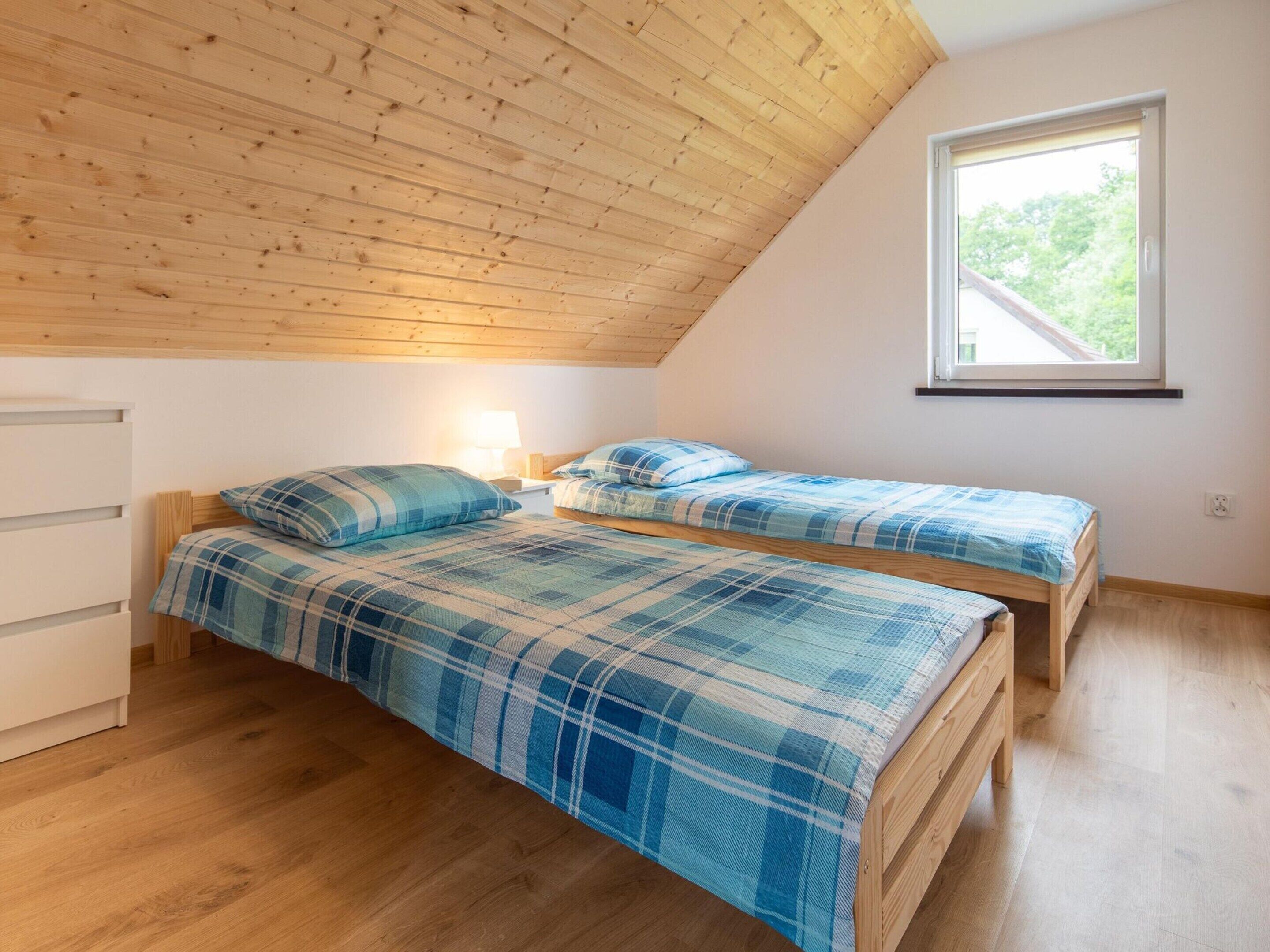 Camera da letto con due letti, soffitto in legno, una finestra e un comodino con una lampada.