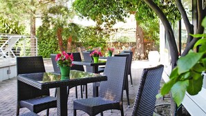 An outdoor seating area with wicker tables and chairs, surrounded by greenery and trees. - Apartment in Pietra Ligure (Pietra Ligure)