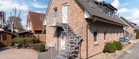 A two-story brick building with a satellite dish, a staircase leading to the upper floor, and a gravel driveway.