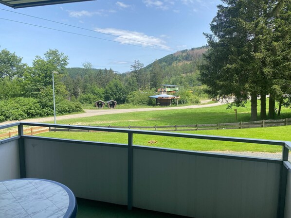 Un balcón con vista a un campo verde, una valla de madera y un edificio con un letrero a lo lejos.