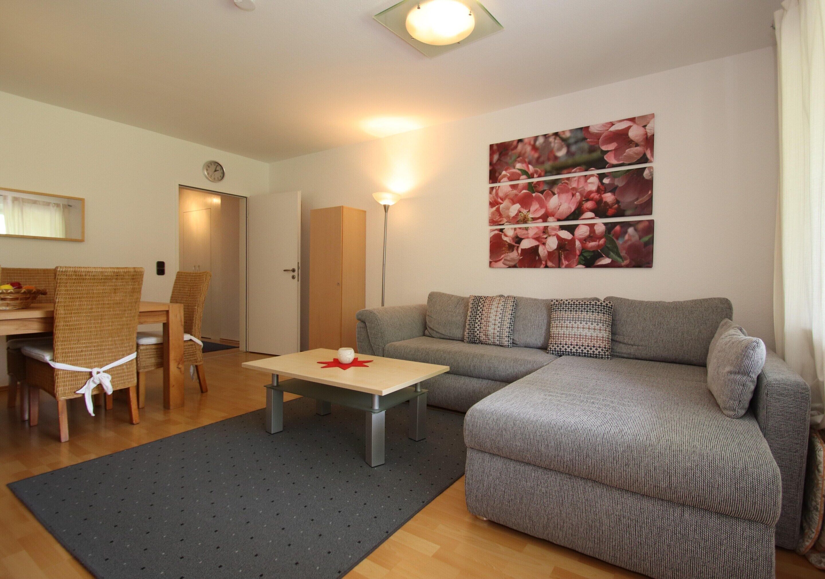 Ein Wohnzimmer mit einer Couch, einem Esstisch mit Stühlen, einem Couchtisch und einem Wandbild.