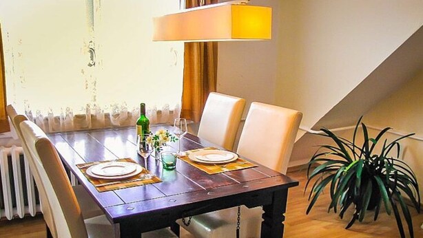 Una mesa de comedor dispuesta con platos, vasos y una botella, rodeada de sillas.