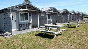 A row of small, single-story cabins with picnic tables in front, each with a door and a small porch area. - Holiday House in Dziwnowek Near Sea and Lake (Kamien Pomorski)