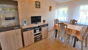 Un coin repas comprenant une table en bois, des chaises, un téléviseur posé sur un meuble et une étagère où sont rangés des verres.
