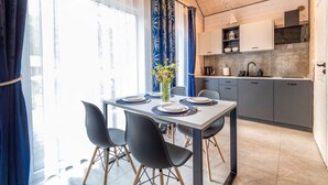 Un comedor moderno con una mesa preparada para cuatro personas, una cocina con armarios grises y un ventanal con cortinas.