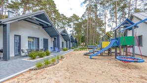 Un edificio moderno con patio, mobiliario exterior y un parque infantil con toboganes y columpios.