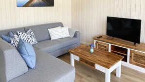 Ein Wohnzimmer mit grauem Sofa, Couchtisch aus Holz und einem Fernseher auf einem Holzschrank.