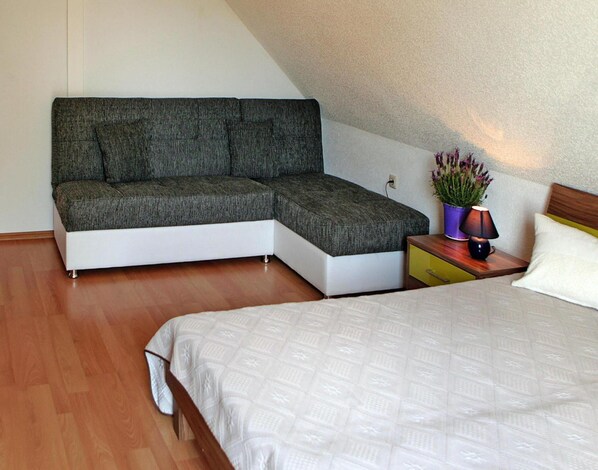 A bedroom with a bed, a corner sofa, a bedside table with a lamp, and a potted plant. - Ferienhauser am Kummerower See, Verchen (Verchen)